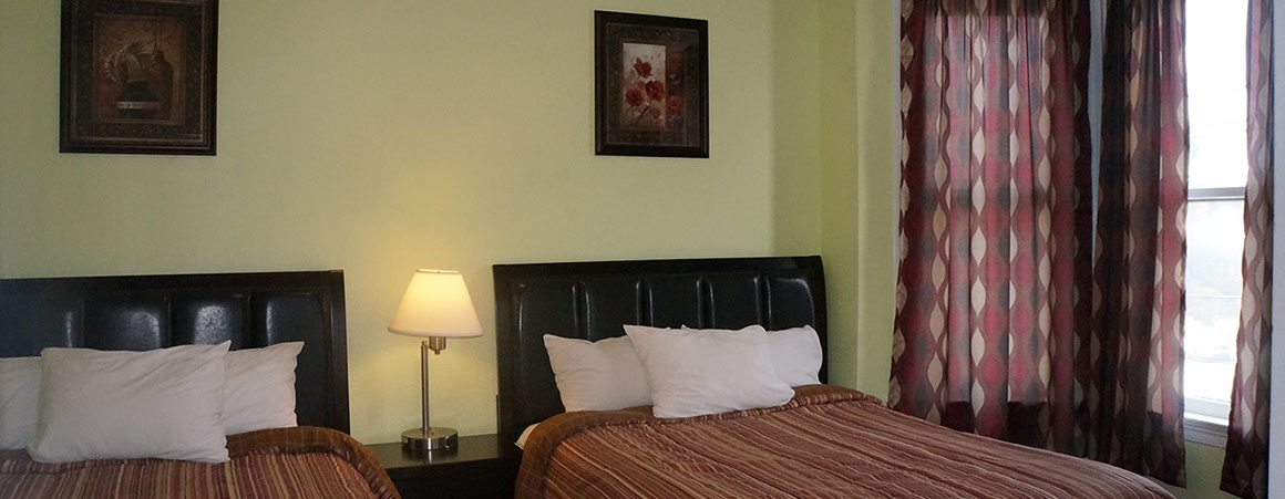 A hotel room with two beds, a nightstand, a lamp, and a window with a curtain.