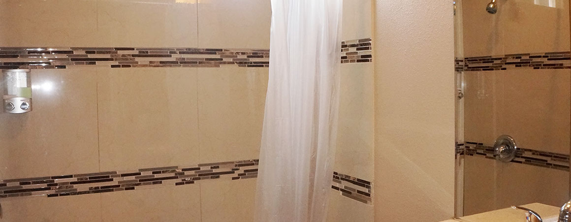 A bathroom shower with beige tiles and a white curtain