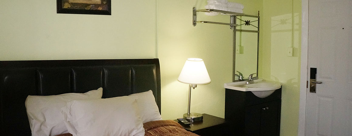 A hotel room with a bed, lamp, sink, and mirror