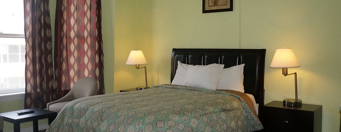 A hotel room with a bed, nightstands, lamps, a window, and a chair.