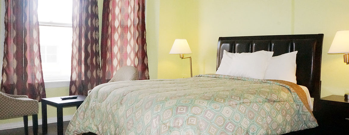 A hotel room with a bed, nightstand, lamp, window, and chair.